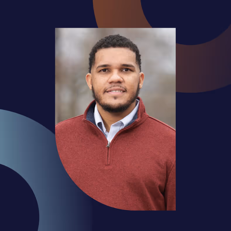 Portrait of a man with short curly hair and beard wearing a red quarter-zip sweater over a light blue collared shirt.
